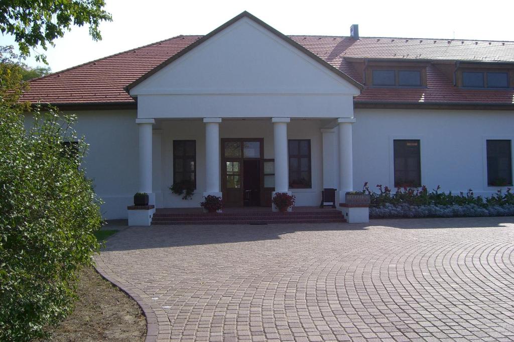 a white house with a brick driveway in front of it at Sarlóspuszta Club Hotel in Tatárszentgyörgy