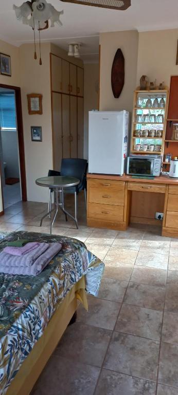 a room with a bed and a table and a refrigerator at Whispering Gardens in Stilbaai