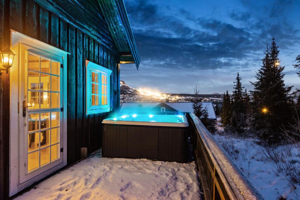 una bañera de hidromasaje al lado de una casa en la nieve en Skeikampen cabin with mountain view, jacuzzi, and 8 bedrooms, en Olstad