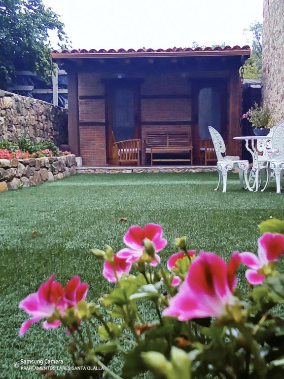 Apartamentos Lares في Santa Olalla: حديقة بها زهور وردية أمام المنزل