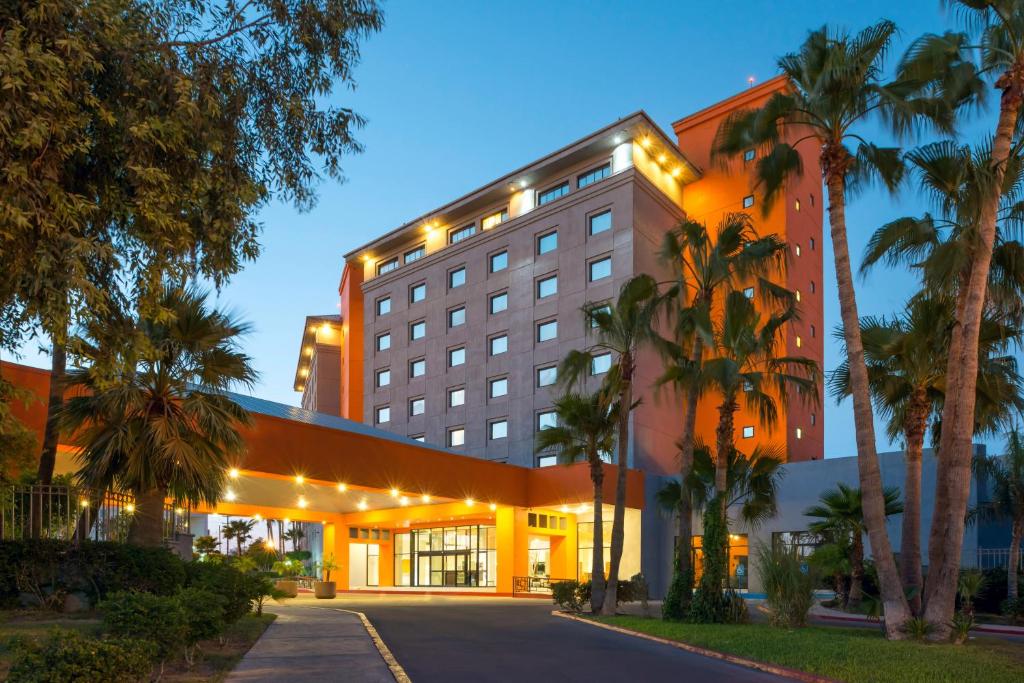 a hotel with palm trees in front of a building at Real Inn Mexicali in Mexicali