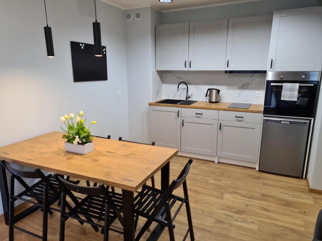 a kitchen with white cabinets and a wooden table with chairs at Apartament Mickiewicza in Puck
