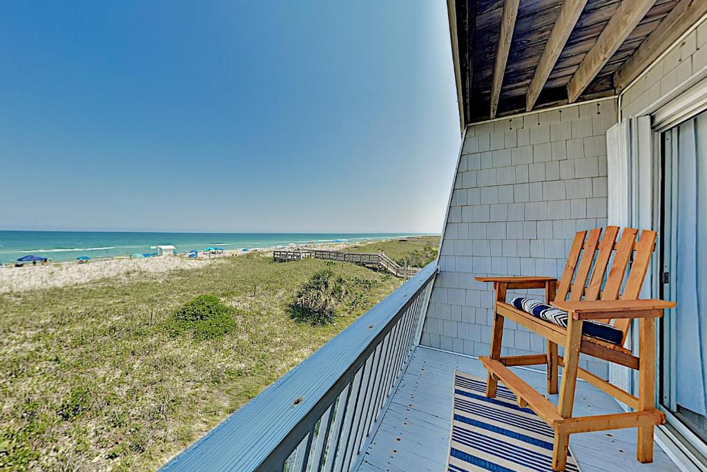 a wooden chair sitting on a porch looking out at the beach at Oceanfront Townhouse in Carolina Beach