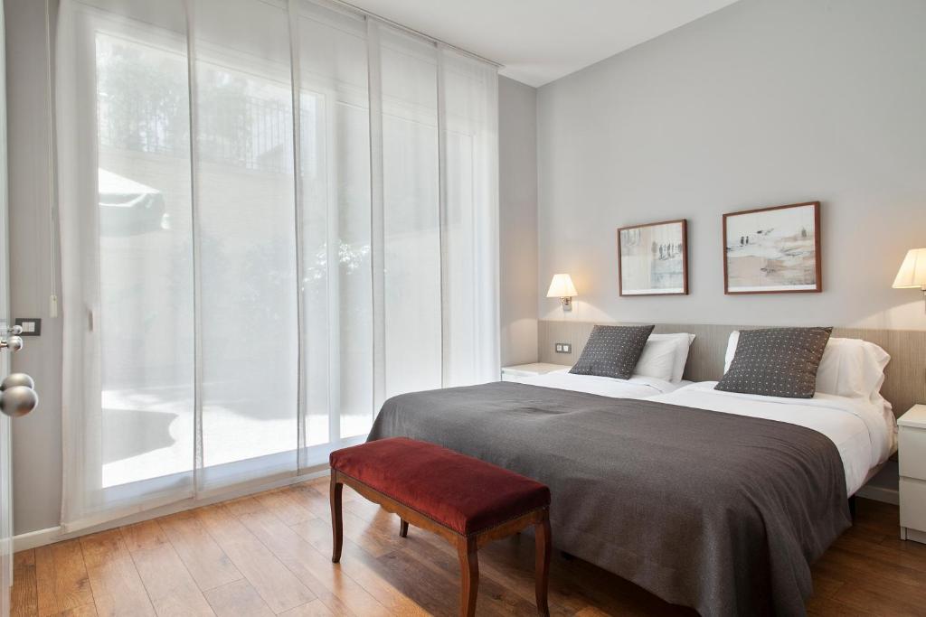 a white bedroom with a large bed and a red stool at Bonavista Apartments - Passeig de Gracia in Barcelona