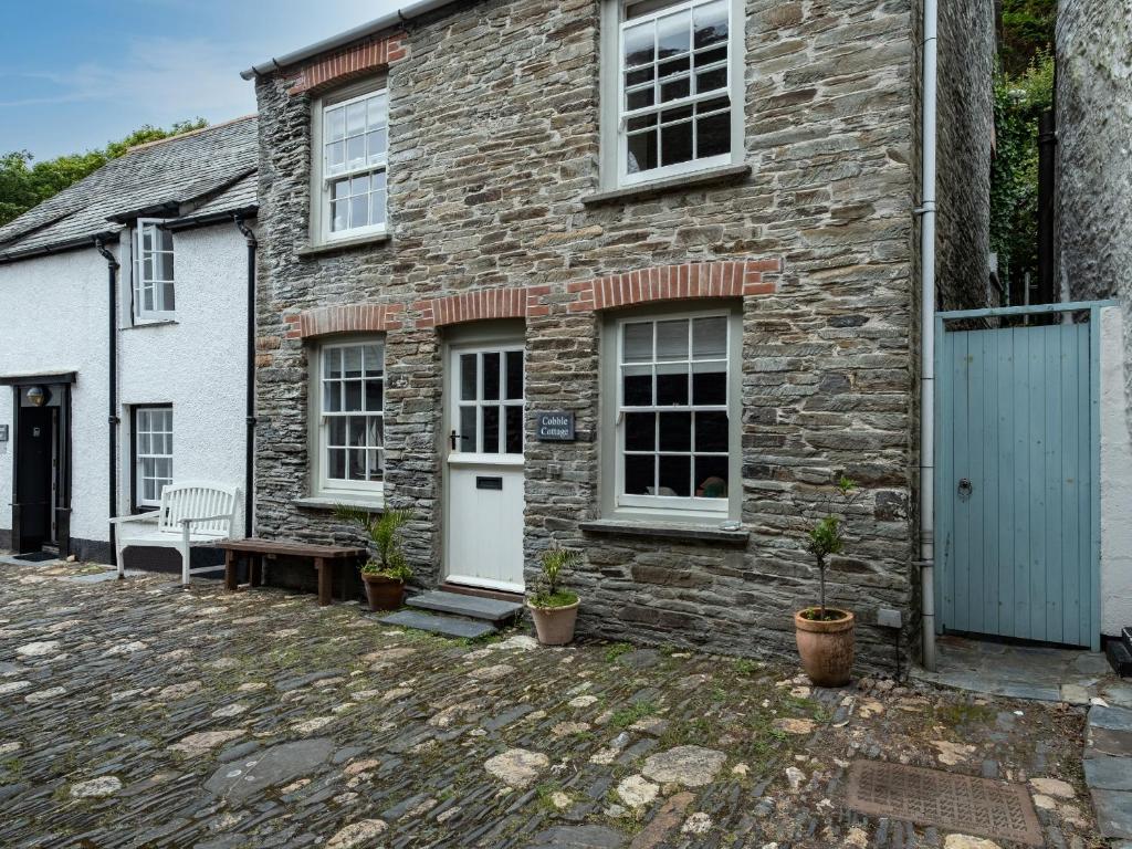 a brick house with a white door and a bench at Cobble Cottage in Boscastle