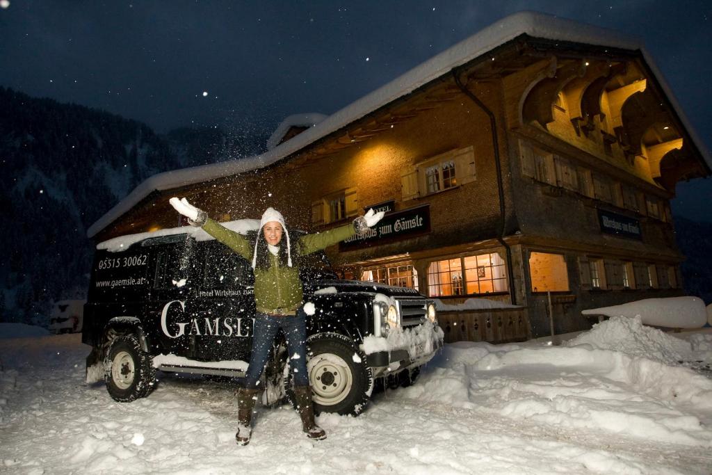 a woman standing in the snow in front of a building at Gämsle Hotel, Wirtshaus & mehr in Schoppernau
