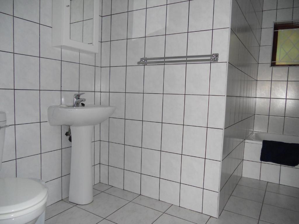 een wit betegelde badkamer met een toilet en een wastafel bij Shore Breakers in Shelly Beach