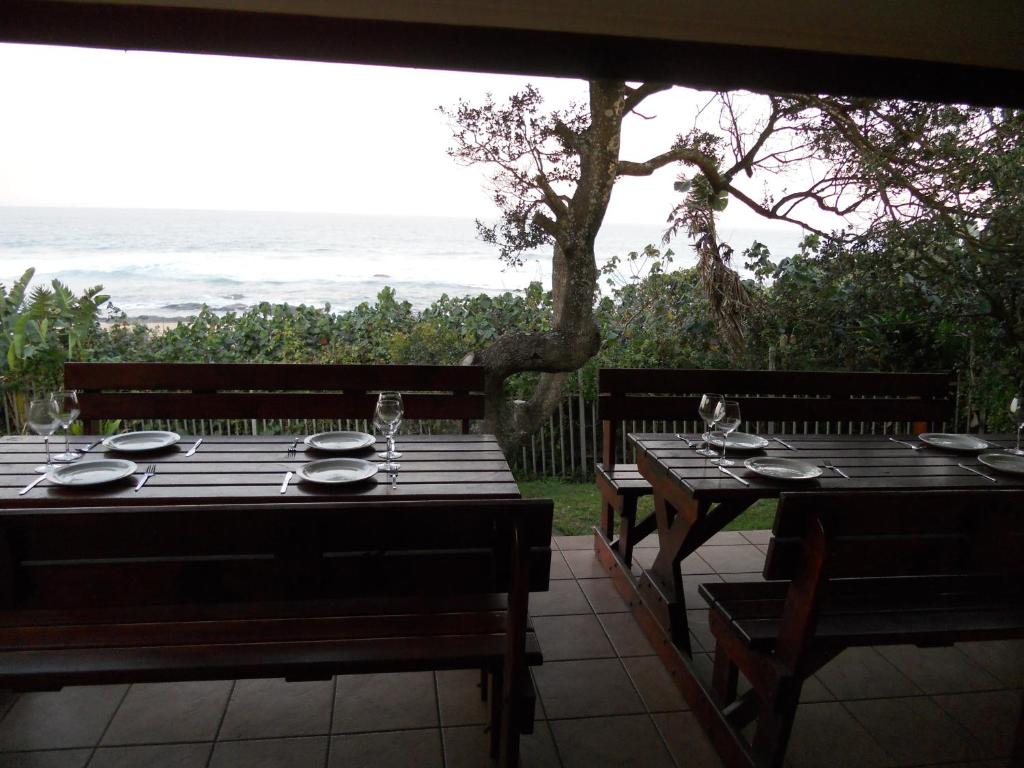 een tafel met borden en wijnglazen op een patio met uitzicht op de oceaan bij Shore Breakers in Shelly Beach