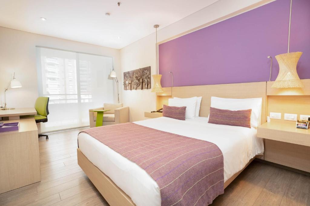 Habitación de hotel con cama grande y pared morada en Hotel Bari Bucaramanga en Bucaramanga