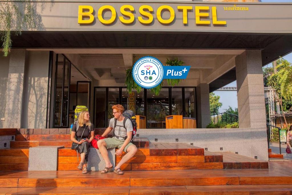 two people sitting on steps in front of a business at Bossotel Chiang Mai - SHA Plus in Chiang Mai