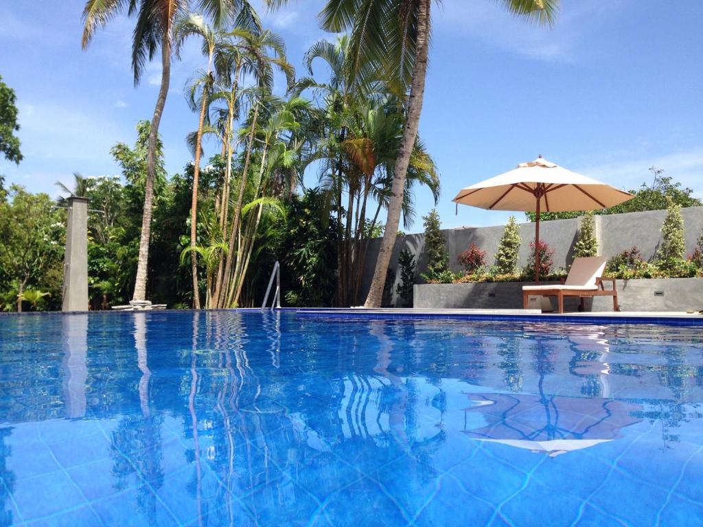 uma piscina com uma cadeira e um guarda-sol em TROPICAL HOUSE - Jungleside Villa em Hikkaduwa