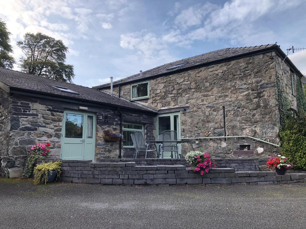 een stenen cottage met een veranda met stoelen en bloemen bij Hafan Cottage at Bryn Llys in Bethesda