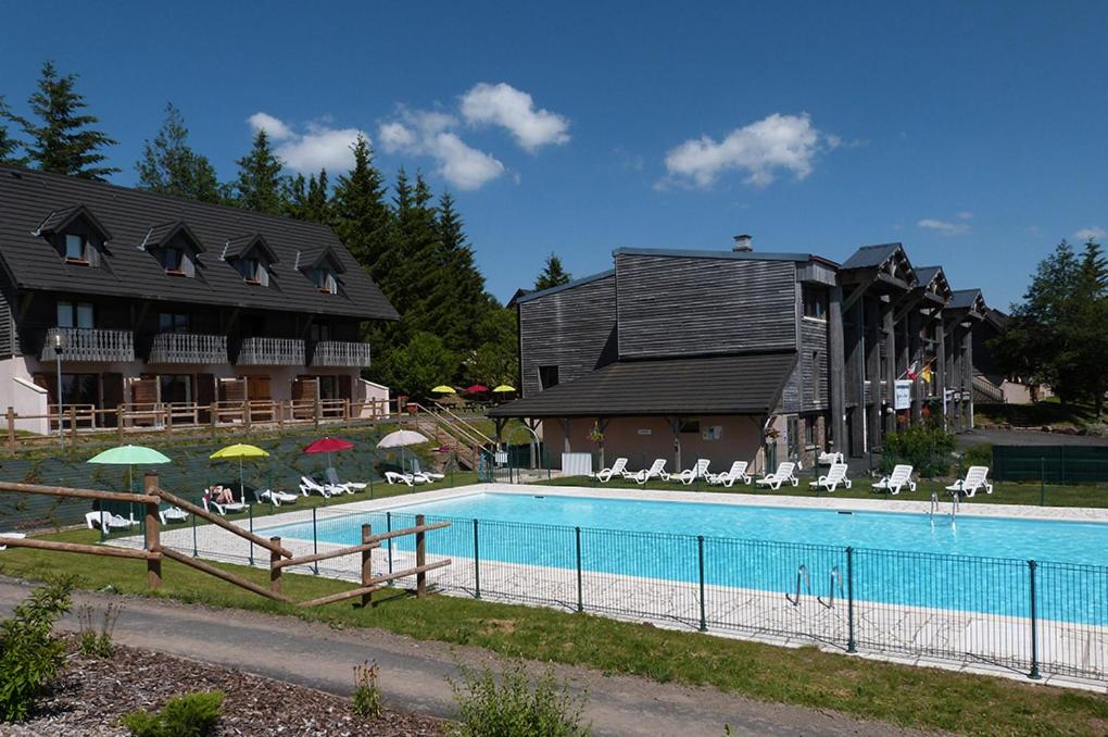 uma piscina com cadeiras e guarda-sóis em frente a um edifício em Grand studio 6 pers. Super Besse, Résidence *** em Besse-et-Saint-Anastaise