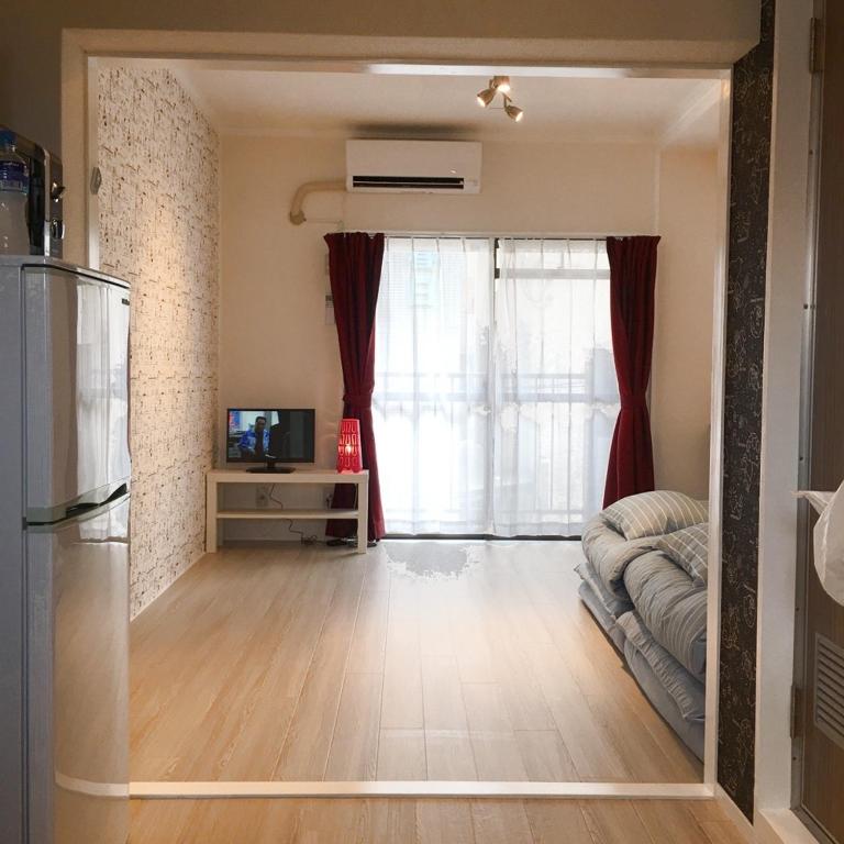 Elle comprend un salon avec un canapé, une télévision et un réfrigérateur. dans l'établissement Guest House Fukuoka W202, à Kasugabaru