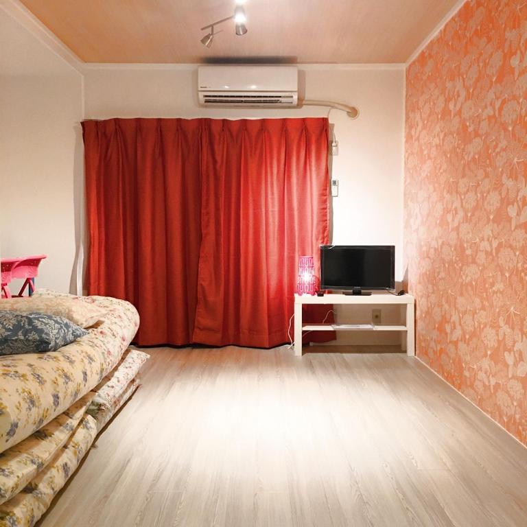 a bedroom with a red curtain and a television at Guest House Fukuoka W303 in Kasuga