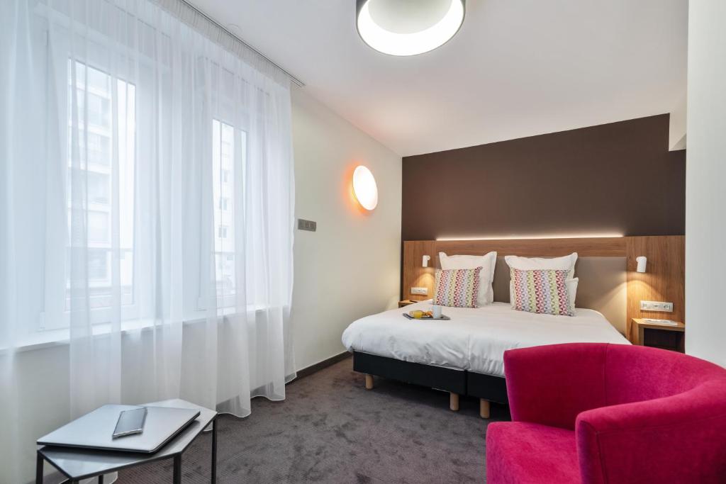 a bedroom with a large bed and a pink chair at Campanile Epinal Centre - Gare in Épinal