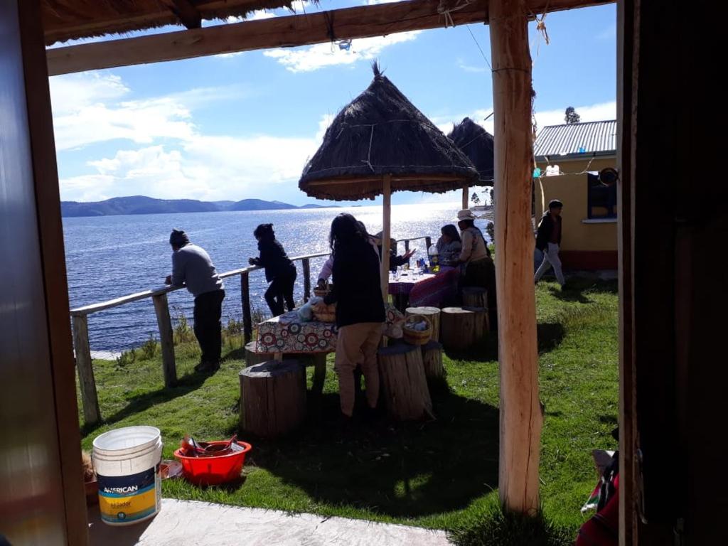 Hostal Luna del Titikaka en Isla de la Luna Bolivia في Isla de la Luna: مجموعة أشخاص يجلسون على طاولة تحت مظلة
