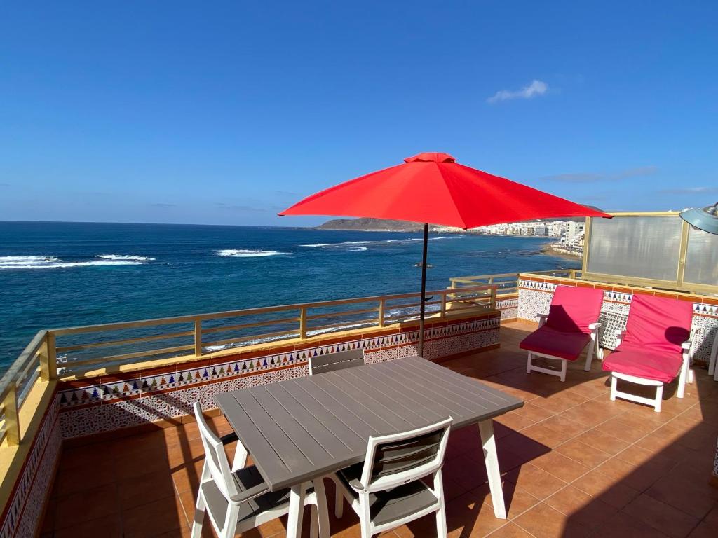 una mesa y sillas con una sombrilla roja en el balcón en Los Gueldes, en Las Palmas de Gran Canaria