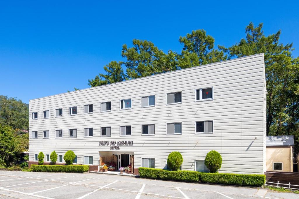 a white building with trees in the background at Hakuba Hotel Paipu no Kemuri in Hakuba