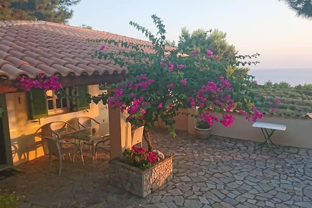 a house with a table and chairs and purple flowers at Villa Angela, Panoramablick übers Meer in Vasilikos