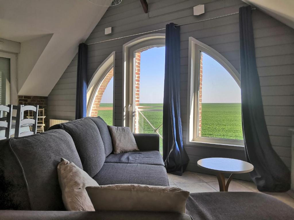 un salon avec un canapé et deux grandes fenêtres dans l'établissement Le Champêtre, à Camblain-lʼAbbé