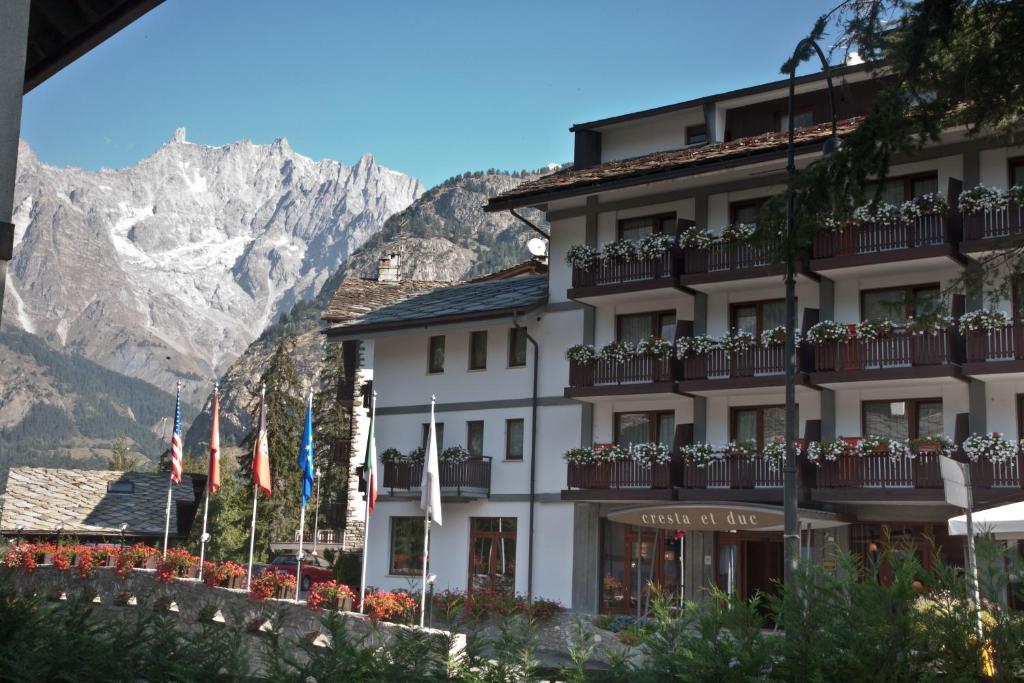 um hotel com bandeiras em frente a uma montanha em Cresta Et Duc Hotel em Courmayeur