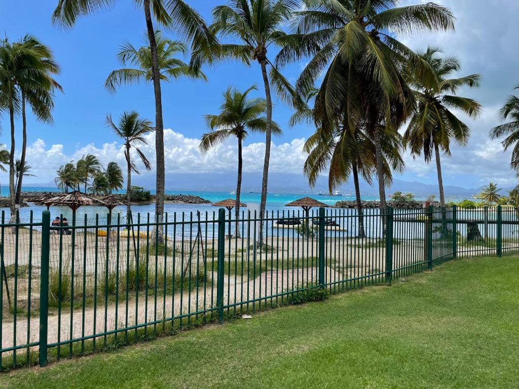 a fence in front of a beach with palm trees at Cauris Lodge du Marisol vue mer accès direct plage in Le Gosier