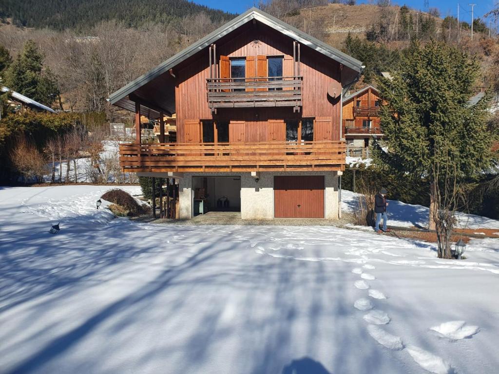 Chalet 8-10 personnes Auris en Oisans Domaine de l'Alpe d'Huez في أوري: منزل خشبي في الثلج مع ممر