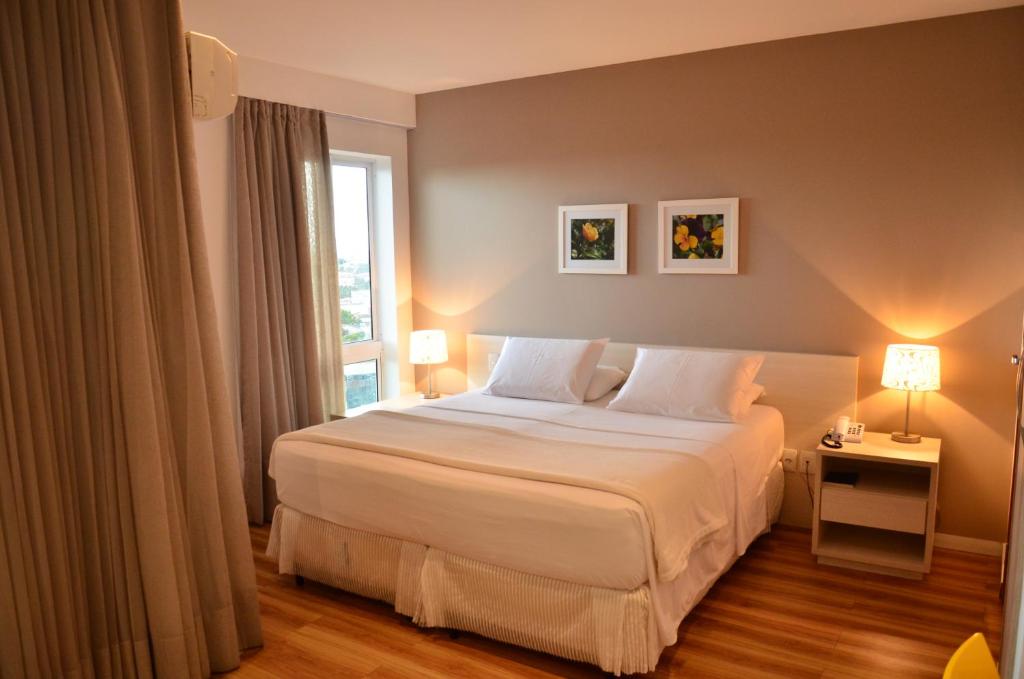 a bedroom with a white bed and a window at Unico Apart Hotel in Feira de Santana