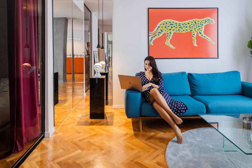a woman sitting on a blue couch with a laptop at Etern Stays - Boutique Apartment in Pristina
