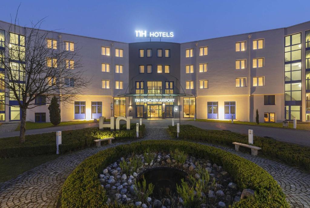 un edificio de hotel con un jardín delante de él en NH München Airport en Oberding