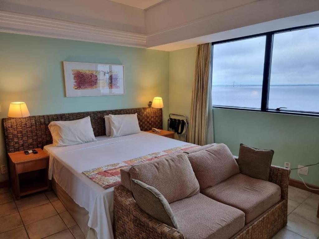 a bedroom with a bed and a couch and a window at Tropical Executive Flat Vista Maravilhosa do Rio in Manaus