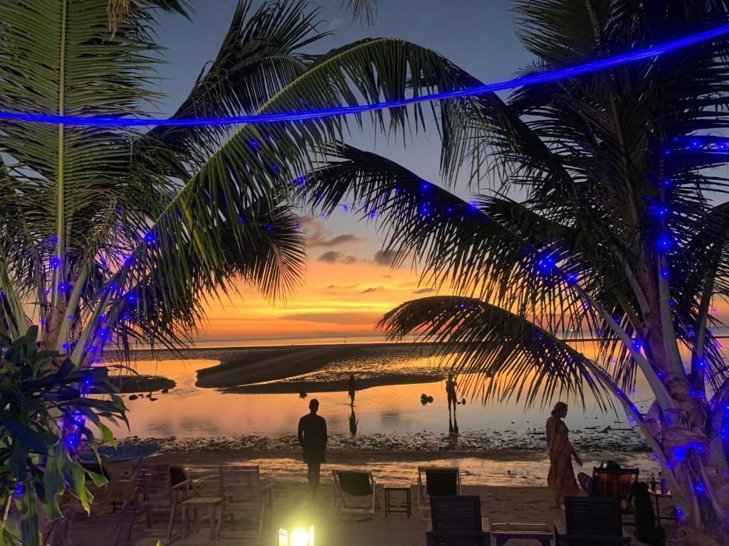 un par de personas de pie en una playa con una puesta de sol en Free Concept Beach Resort, en Srithanu