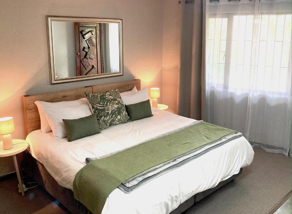 a bedroom with a large bed with green and white pillows at Aloe Cottage in Nelspruit