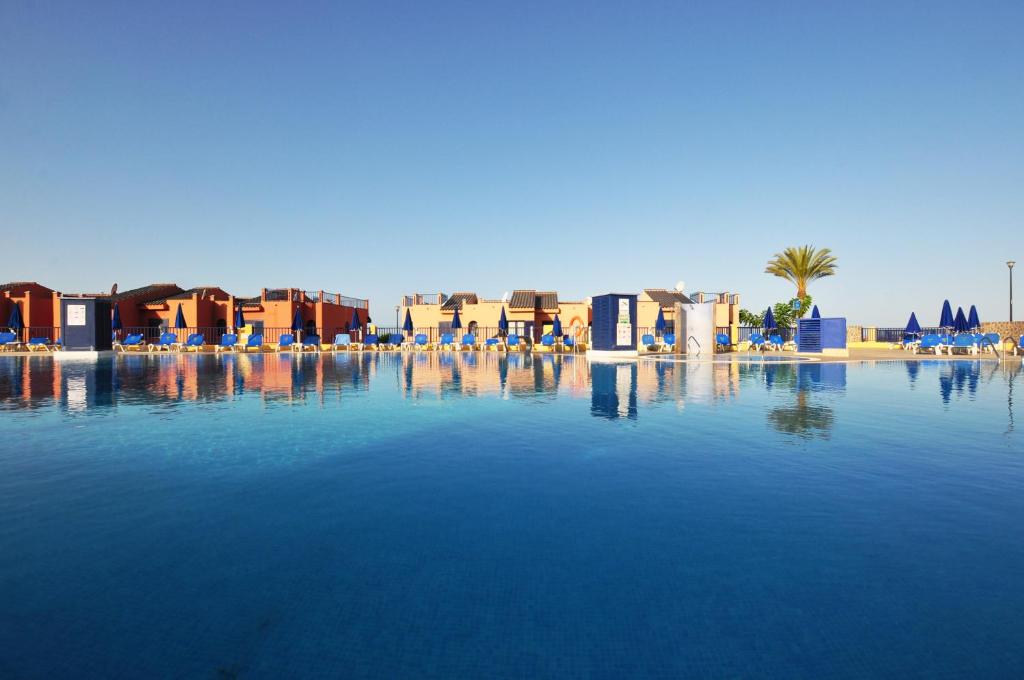 a large pool of water with chairs and buildings at Meloneras Sunset in Meloneras