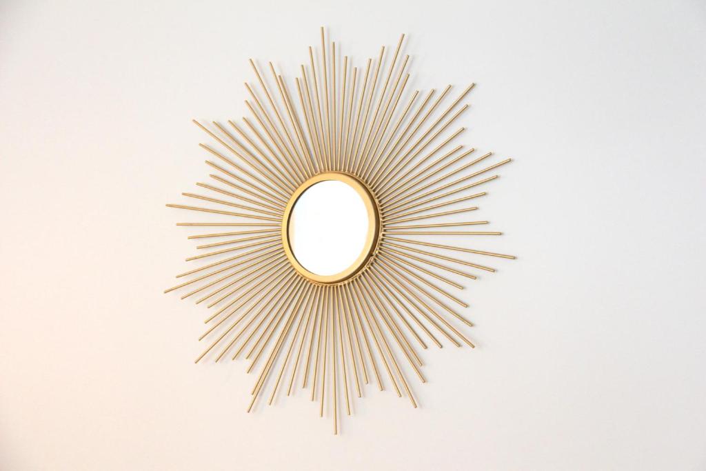 a gold sunburst mirror on a white wall at Le Lac d&#39;Or - Duke Housing in Créteil