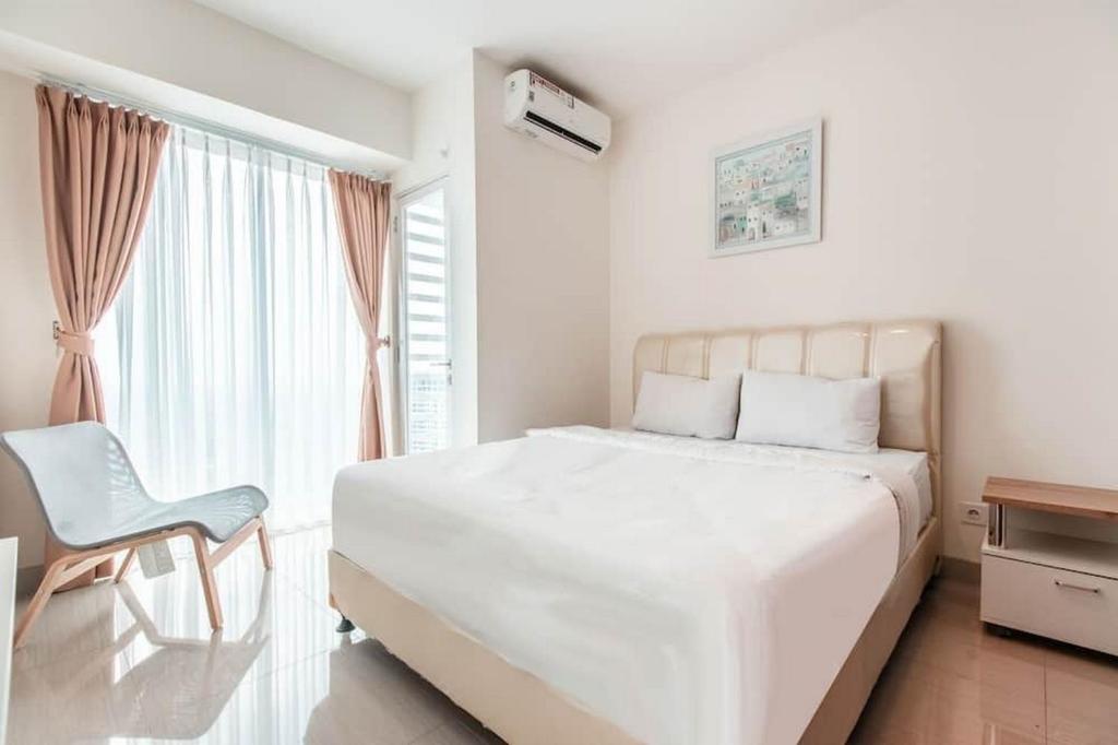 a white bedroom with a large bed and a chair at RedLiving Apartemen Grand Kamala Lagoon - Kita Pro Tower Barclay North in Bekasi