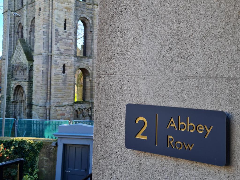 una señal en el lado de un edificio al lado de una iglesia en 2 Abbey Row, en Kelso