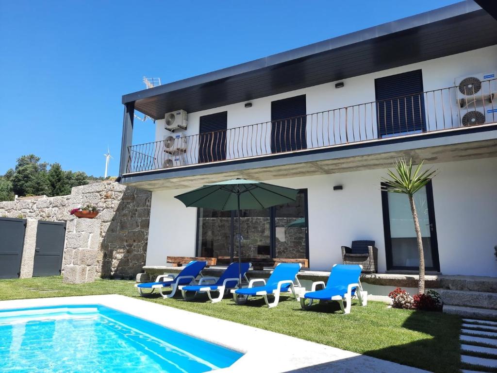 een huis met een zwembad en blauwe stoelen en een parasol bij Casa do Abade - Country House in Viseu