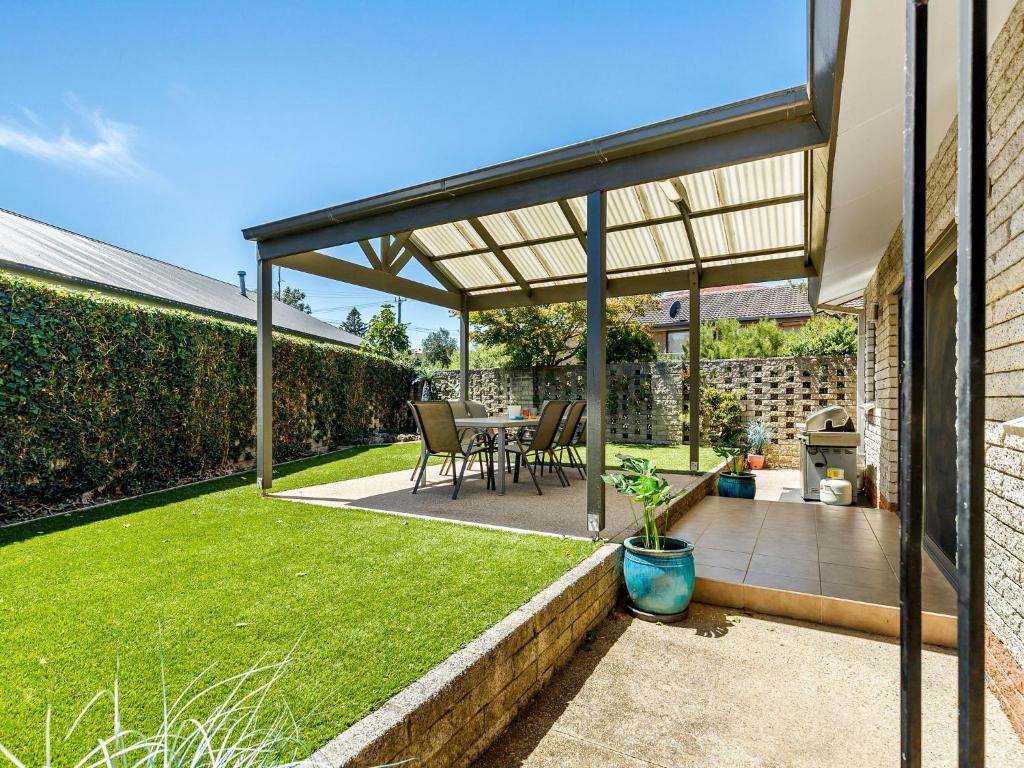 een terras met een tafel en stoelen onder een pergola bij Maybloom in Rye