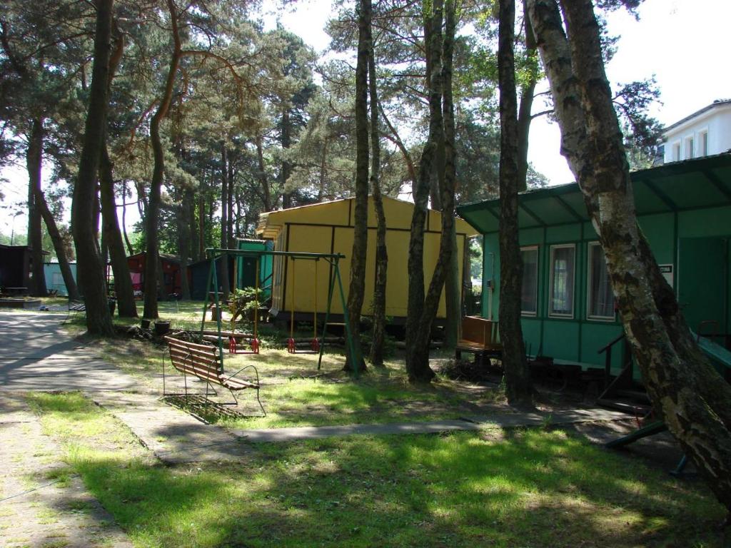 a green and yellow house with a bench and trees at DOMKI SZUMI LAS in Mrzeżyno