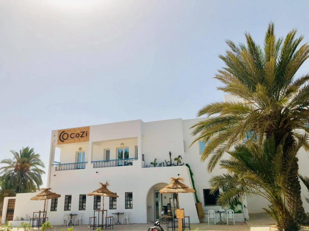 a building with a palm tree in front of it at CoZi Coliving space Djerba in Mezraya