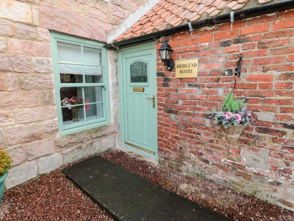 a brick house with a door and a sign that says naughty build at Bridge End Bothy in Wooler