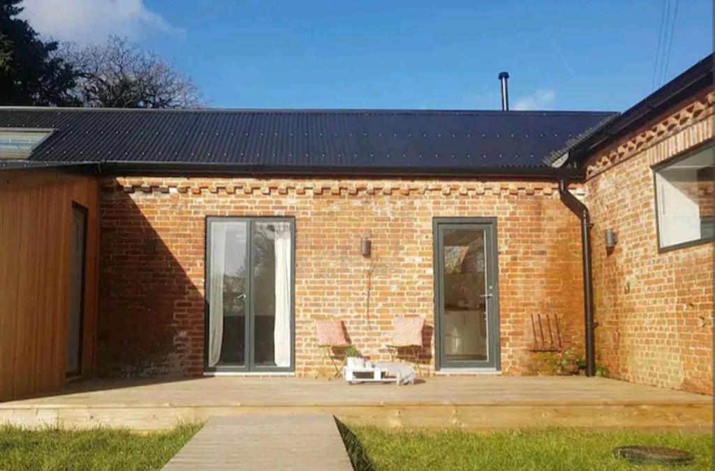 a brick house with a chair on a patio at Super cute and cosy one bedroom barn nr Southwold in Southwold