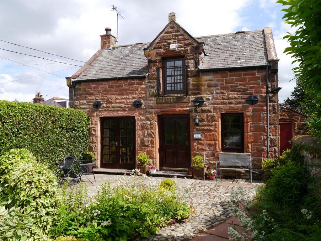 una vieja casa de ladrillo con un jardín delante de ella en Belmont Cottage, en Dumfries