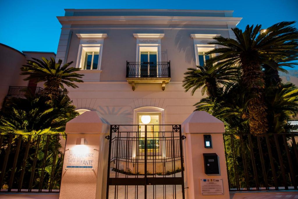een wit huis met een poort en palmbomen bij La Corte del Fante in Marsala