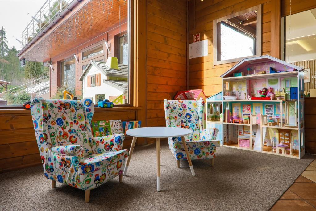 Children's play corner with colorful patterned armchairs, small round table, and large dollhouse.