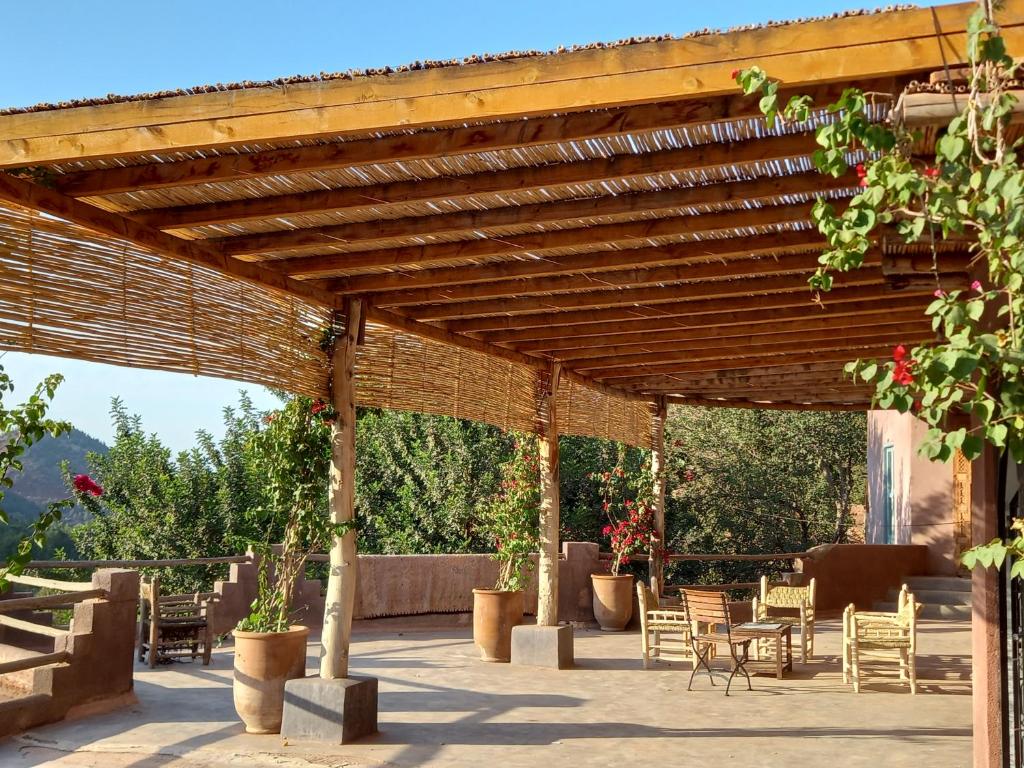 uma pérgola de madeira com cadeiras e mesas num pátio em Ourika Timalizène le jardin des délices em Tamzerdirt