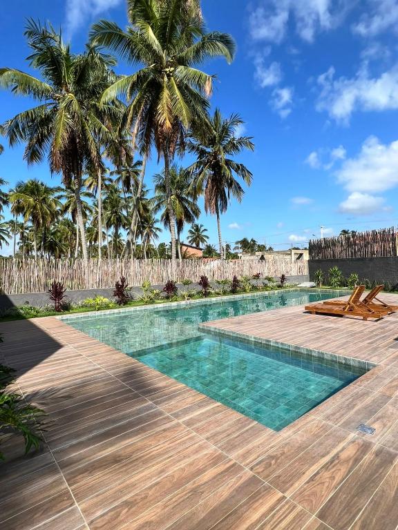 a swimming pool with a wooden deck and palm trees at PATACHO VILLE - Rota Ecológica dos MILAGRES in Pôrto de Pedras