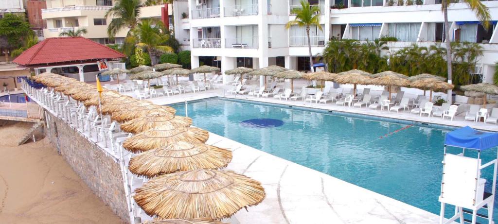 een zwembad met rieten parasols en stoelen naast een gebouw bij Suites Torres Gemelas VIP in Acapulco